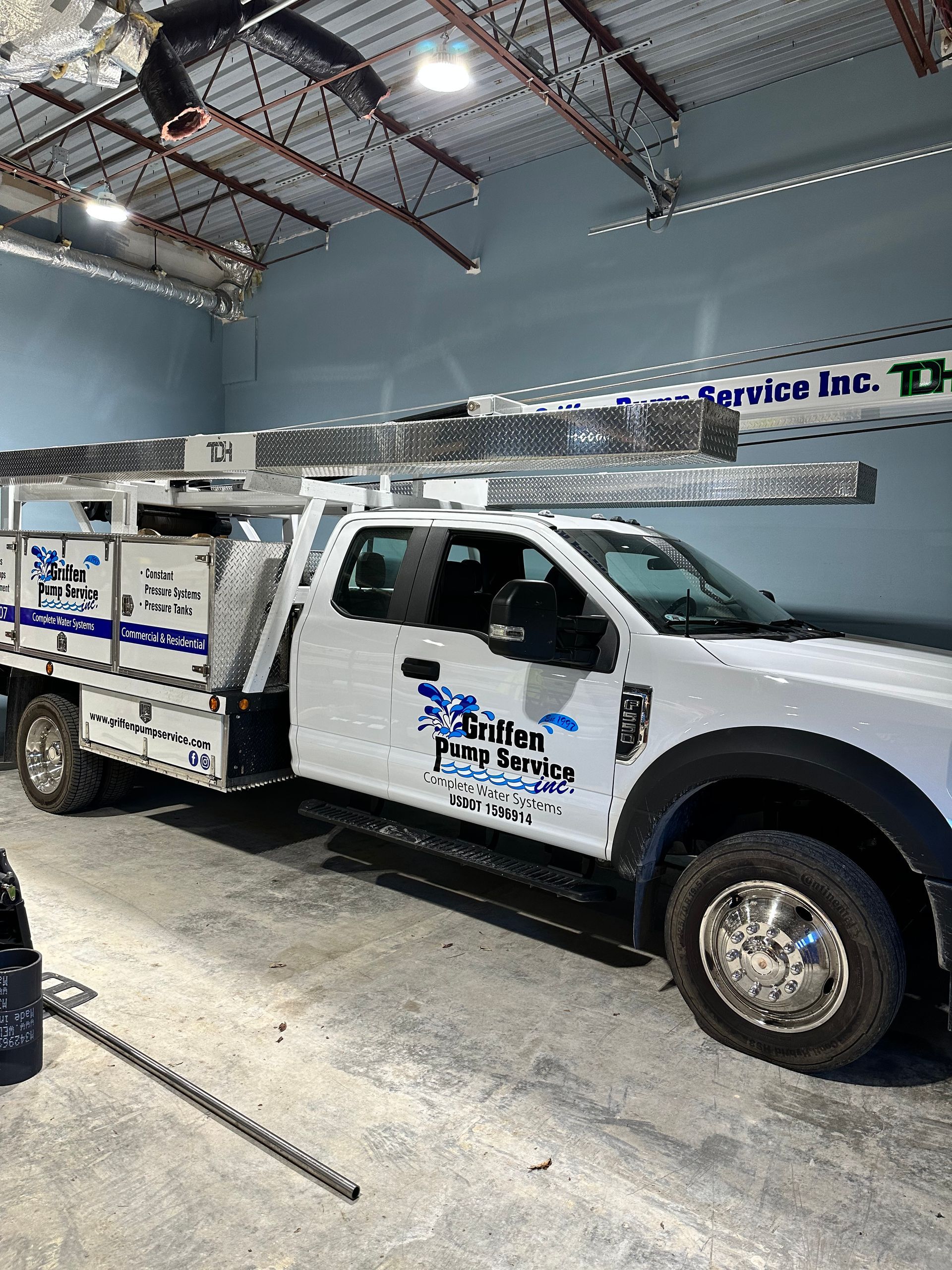 A white truck with a ladder on top of it is parked in a garage.