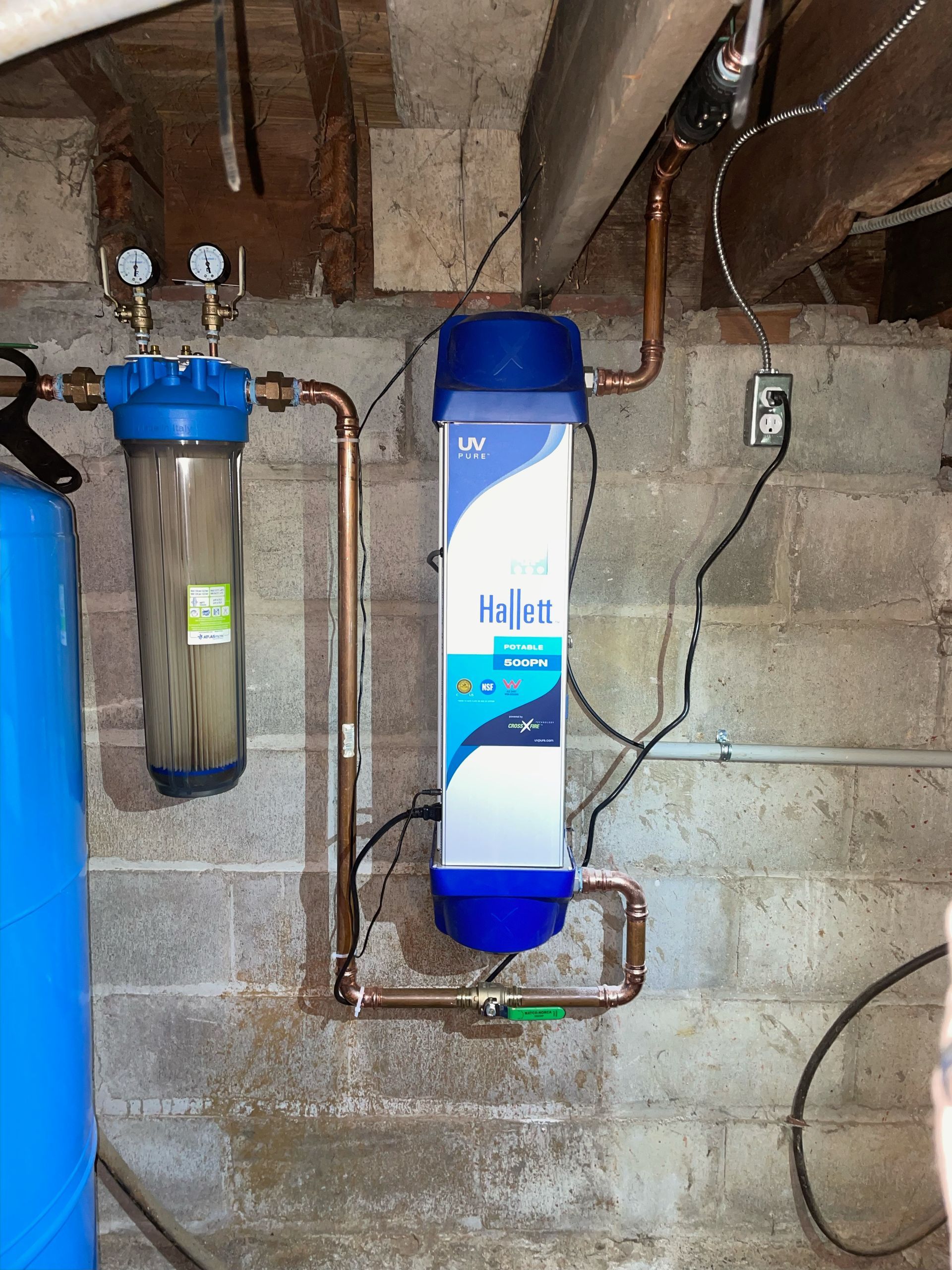 A water filter is attached to a brick wall in a basement.