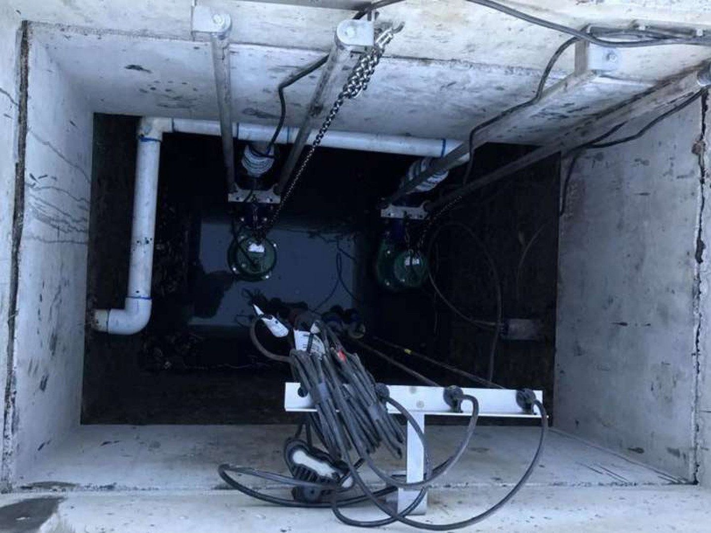 A hole in the ground with pipes and wires coming out of it.