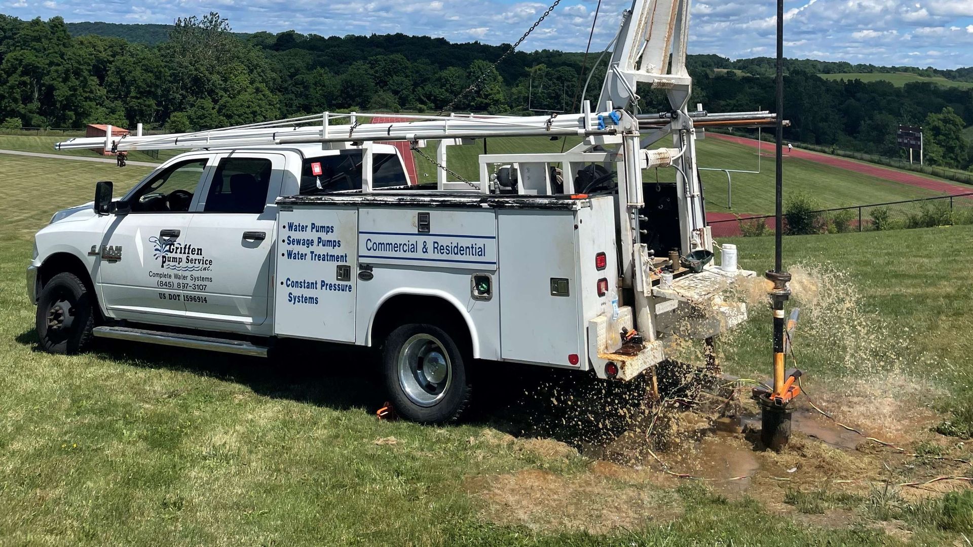 A white truck is drilling a hole in the ground in a field.