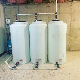 Three white water tanks are sitting next to each other in a basement.