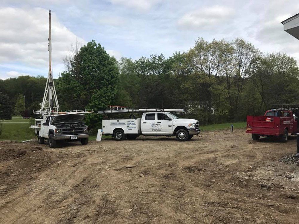 Two trucks are parked in a dirt lot with trees in the background.