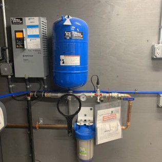 A blue water tank is hanging on a wall next to a water filter.