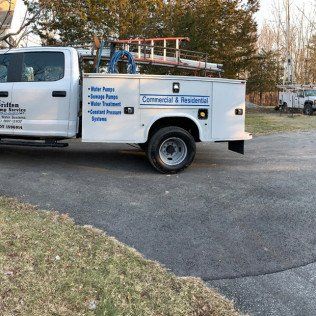 A white truck with a ladder on top of it is parked in a driveway.