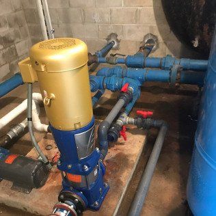 A water pump is sitting on top of a wooden platform surrounded by blue pipes.