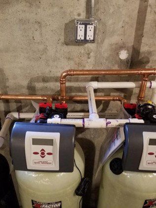 Two water treatment systems are sitting next to each other in a basement.