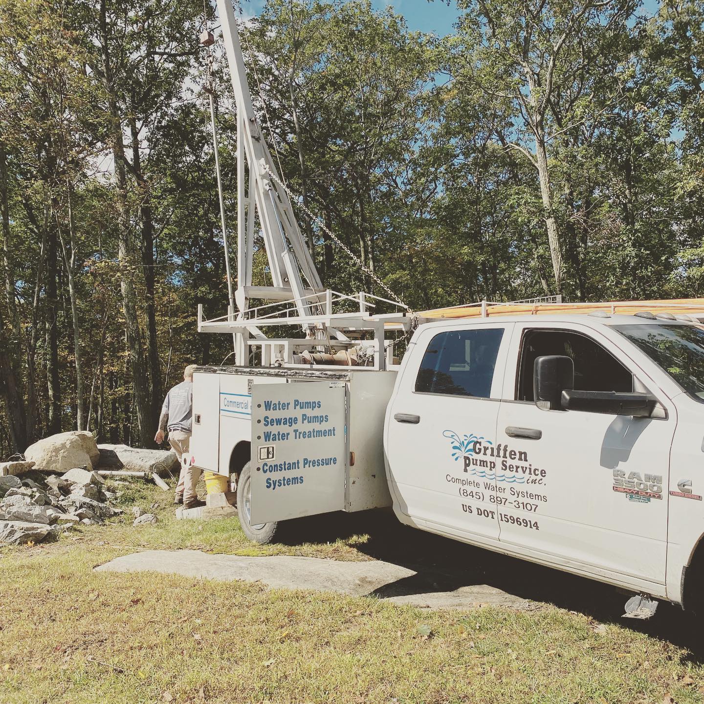A white truck is parked in a grassy field with trees in the background.