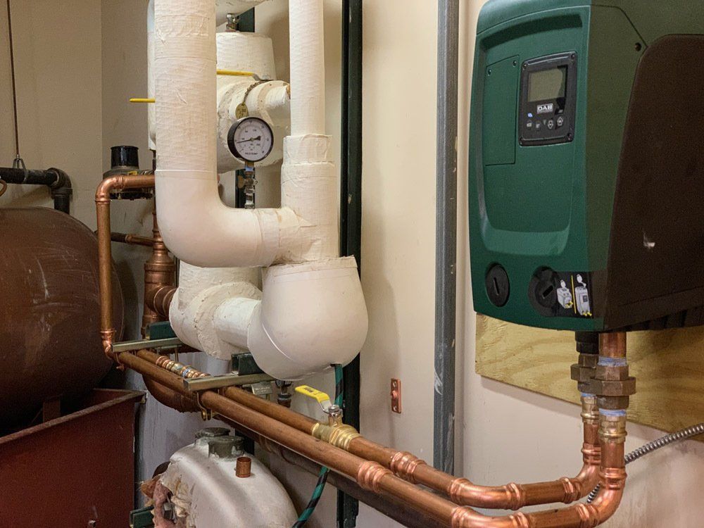 A room with a lot of pipes and a green device on the wall.