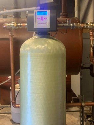 A water softener is sitting next to a boiler in a room.