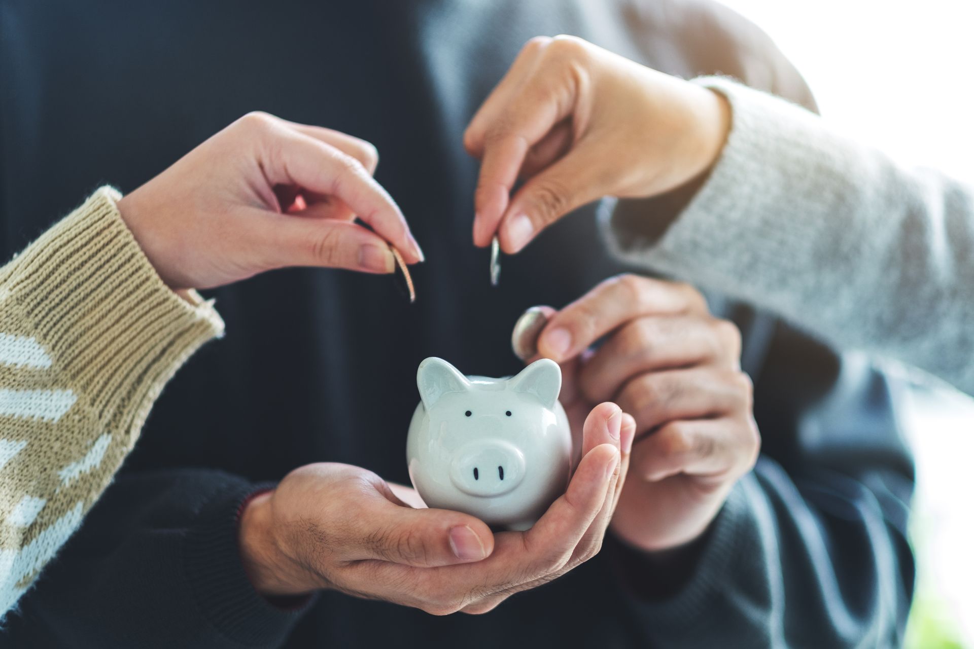 Hands putting coins into a white piggy bank.