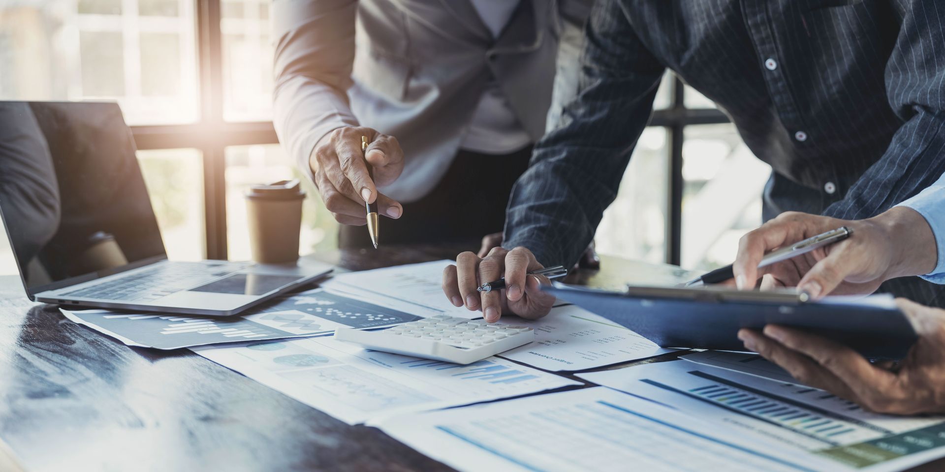 People reviewing documents around a table with a laptop, calculator, and coffee cup.