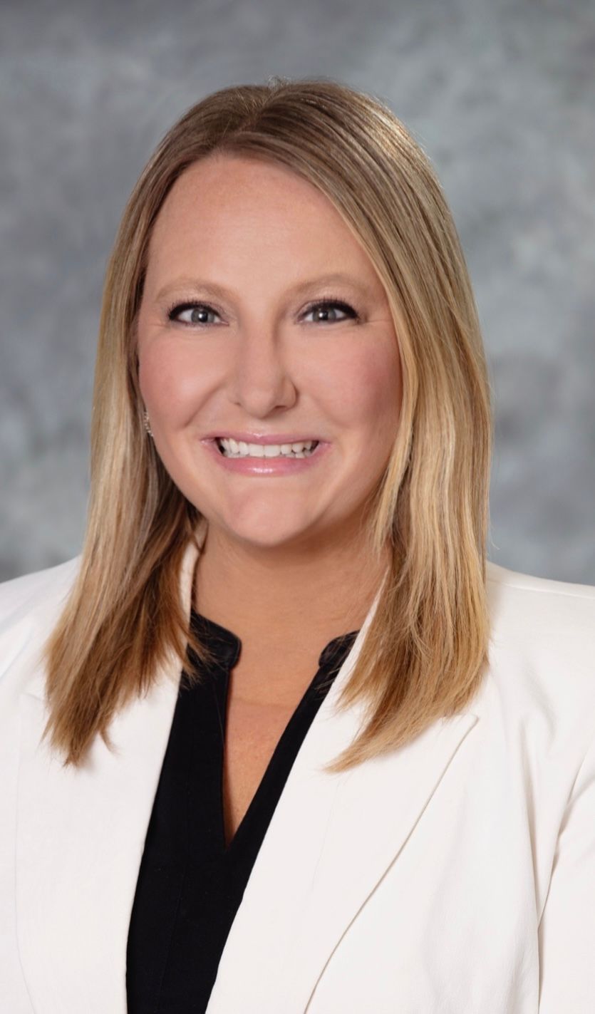 Woman with blonde hair wearing a white blazer, smiling at the camera.