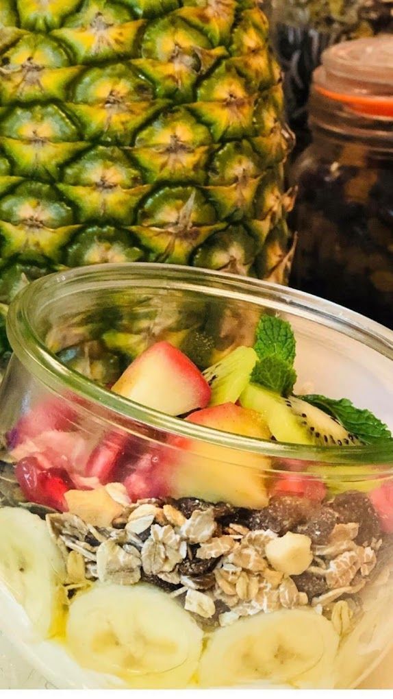 Een glazen kom gevuld met fruit en haver naast een ananas.