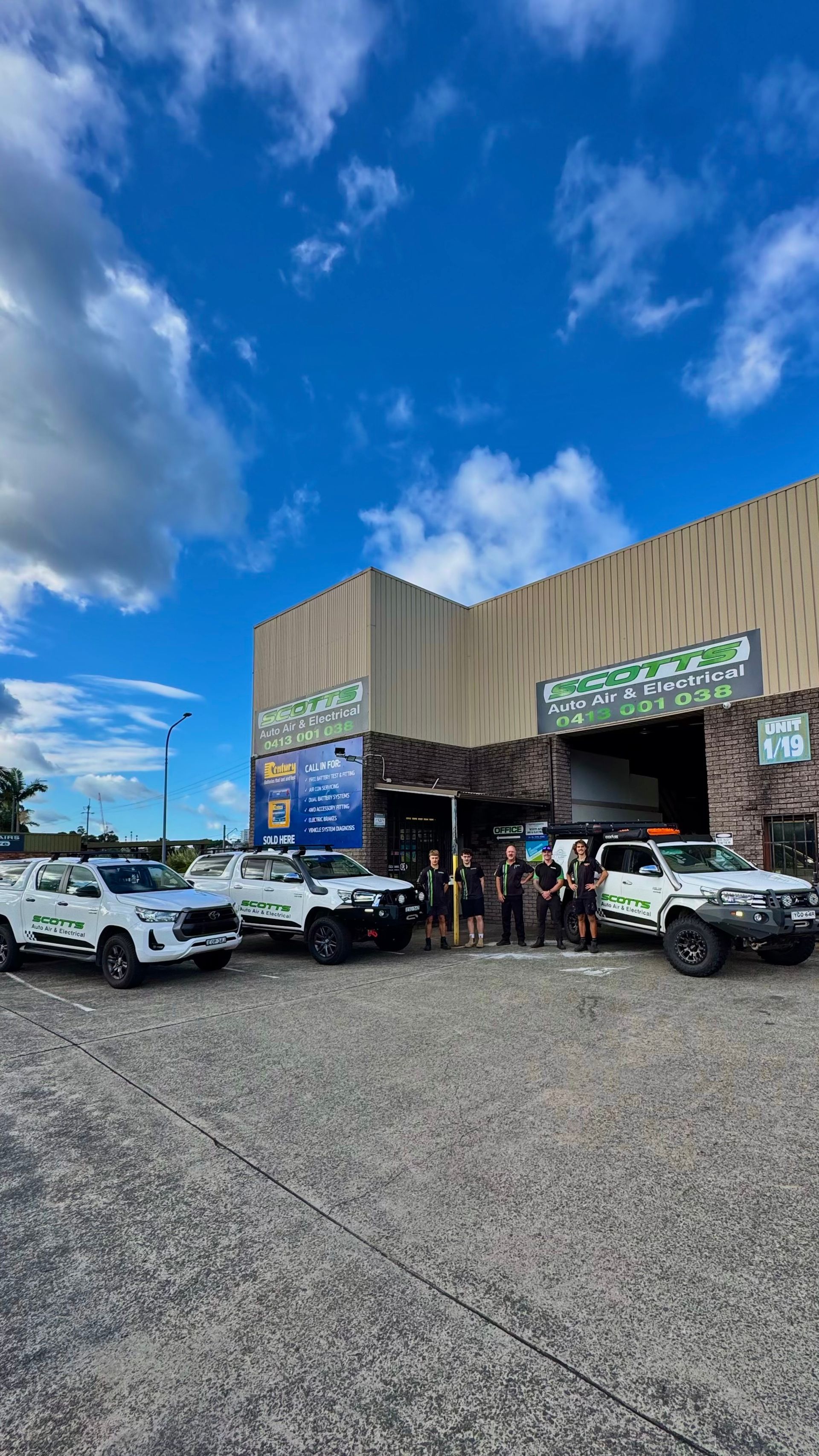 A Mechanic team is standing out front of their workshop with their vehicles — Scotts Auto Air & Electrical In Wollongong, NSW