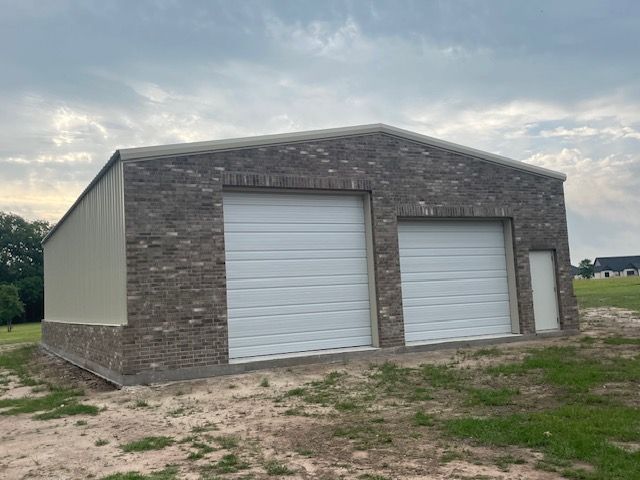 A garage with two white garage doors is sitting in the middle of a field.