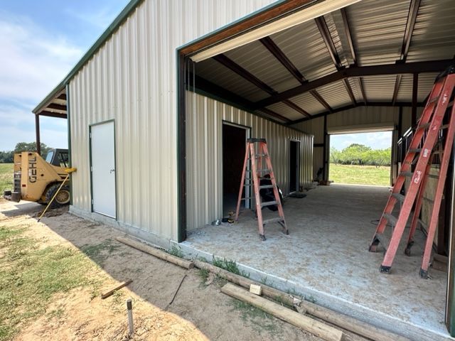 A yellow bulldozer is parked in front of a metal building under construction.