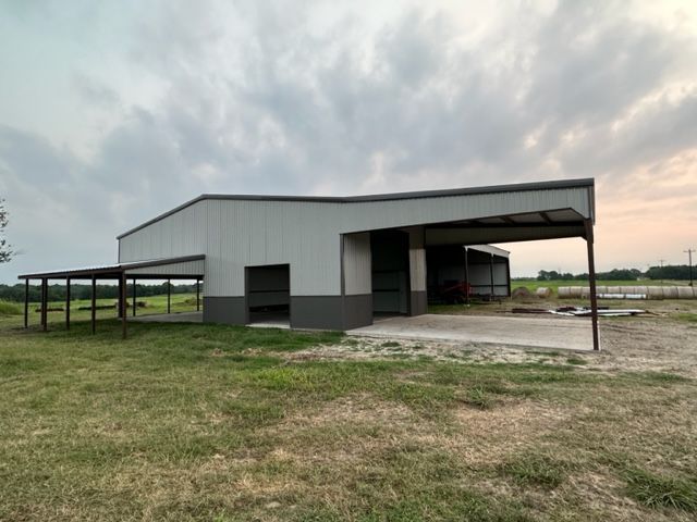 A large metal building with a carport attached to it is sitting in the middle of a grassy field.