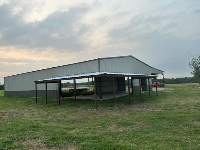A large metal building with a covered area in the middle of a grassy field.
