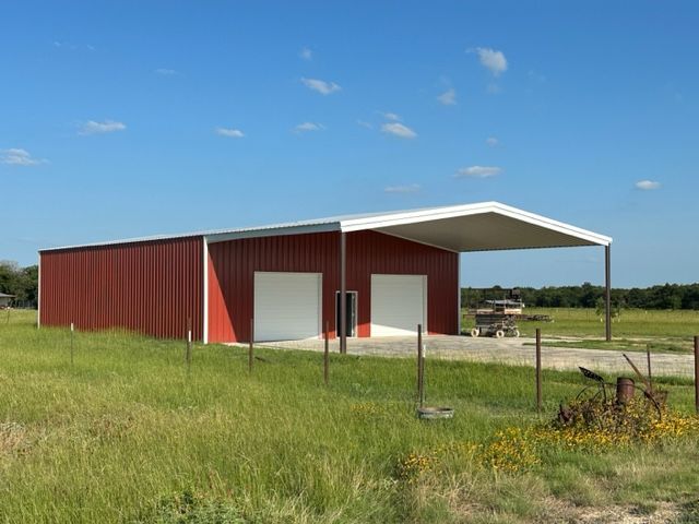 A red barn with a white roof is in the middle of a grassy field.