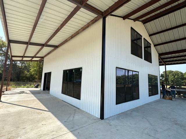 White metal building with black-framed windows, under a brown metal roof. Outdoors, concrete patio.