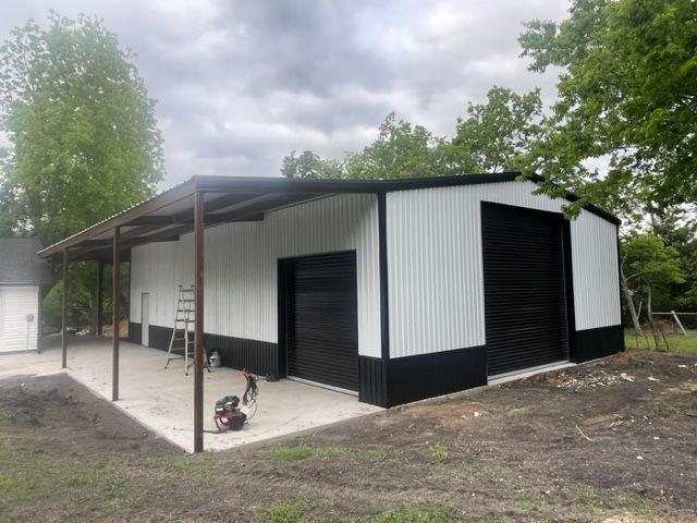 A white and black metal building with a covered porch and a garage door.