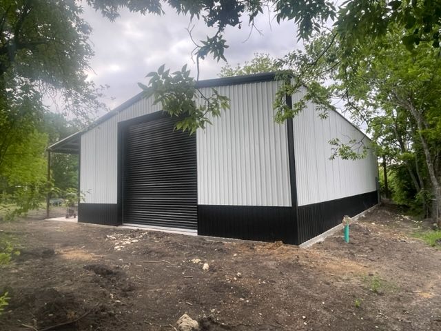 A white metal building with a black door is sitting in the middle of a dirt field.