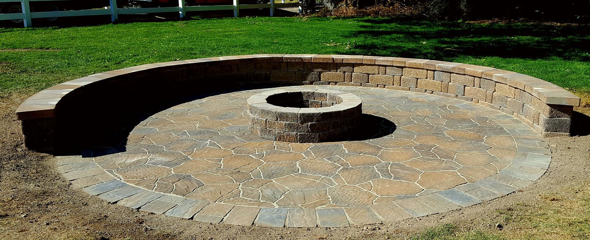 A fire pit is surrounded by a stone wall and a bench.