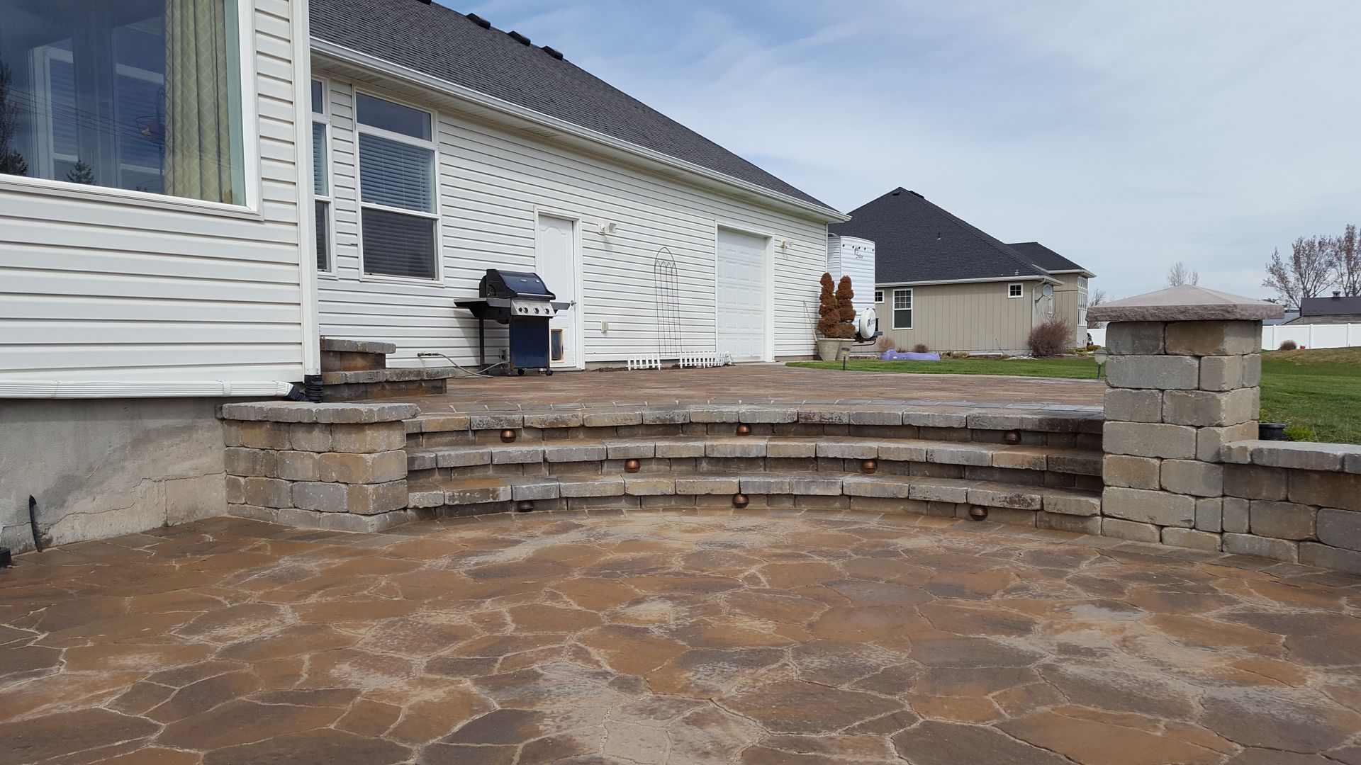 A patio with stairs and a grill in front of a house.