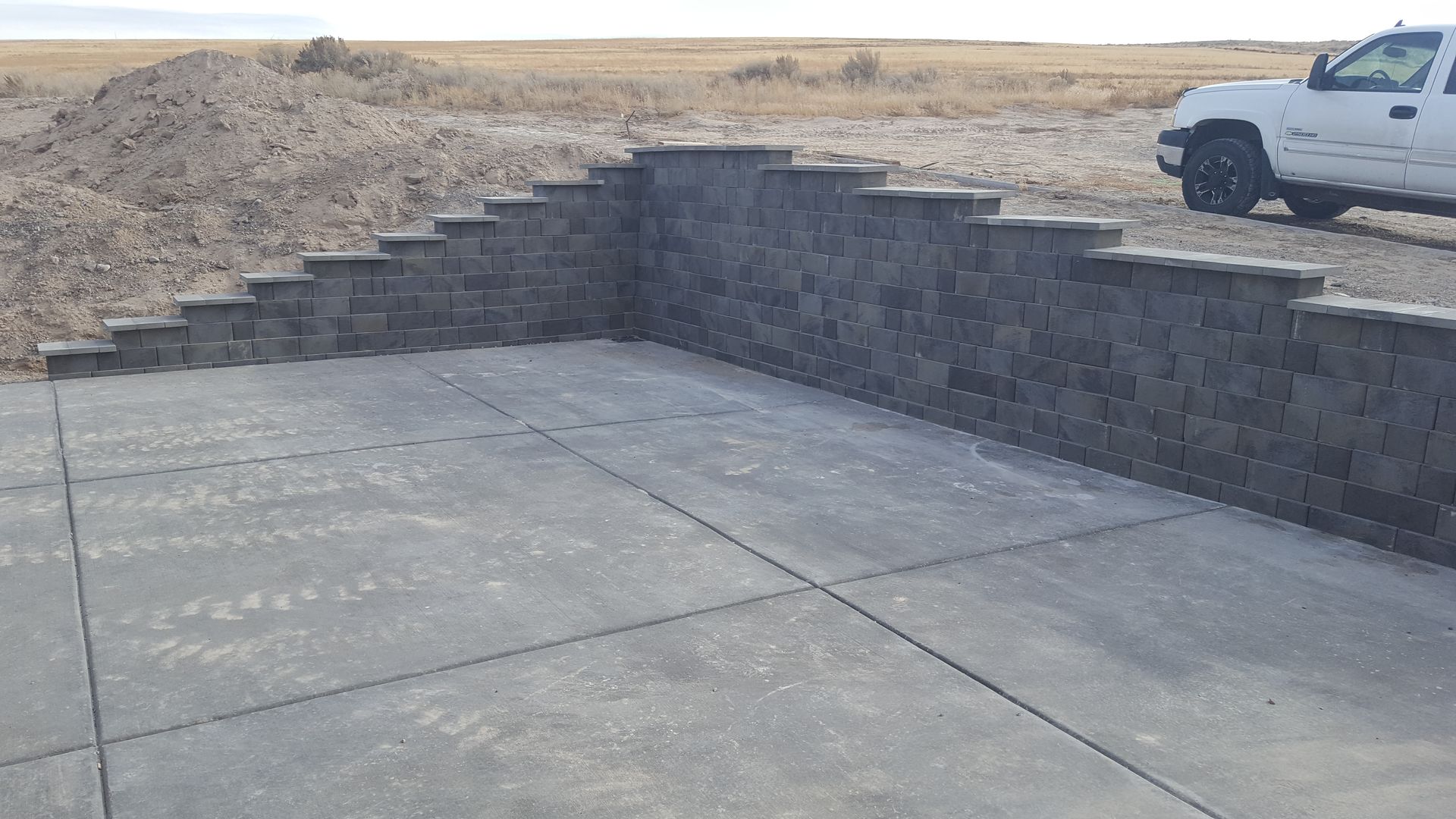 A white truck is parked in front of a concrete wall.