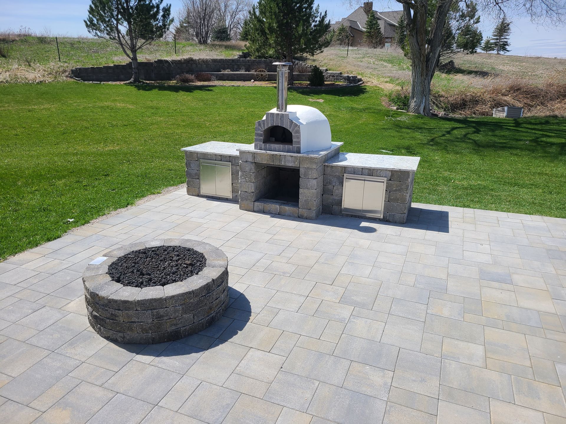 A pizza oven is sitting next to a fire pit on a patio.