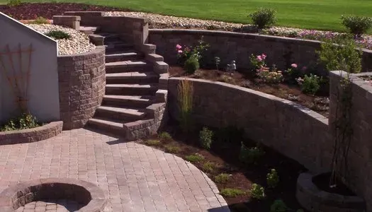 A stone wall with stairs leading up to a patio and a fire pit.