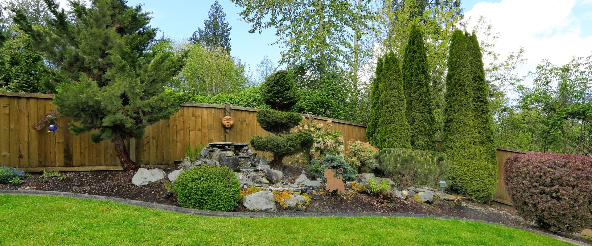 A lush green lawn with a wooden fence and trees in the background.