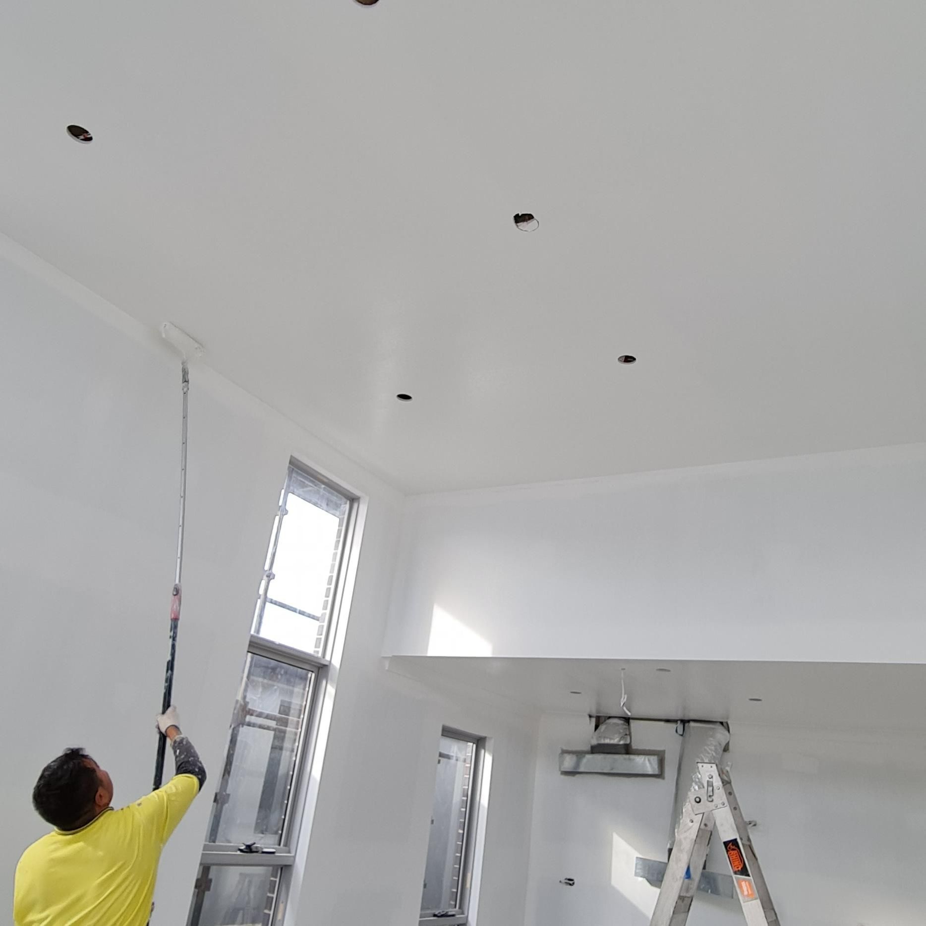 A Man In A Yellow Shirt Is Painting The Ceiling Of A Room — Blue Painting & Decorating In Taylor, ACT