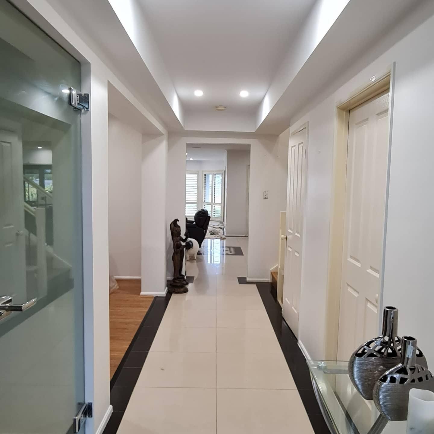 A Long Hallway With A Glass Door And Vases On The Floor — Blue Painting & Decorating In Taylor, ACT