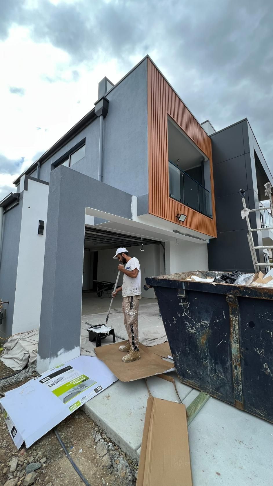A Man Is Standing In Front Of A Large House Under Construction — Blue Painting & Decorating In Taylor, ACT