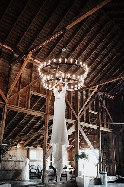 beautiful bride dress hanging from chandelier in rustic barn