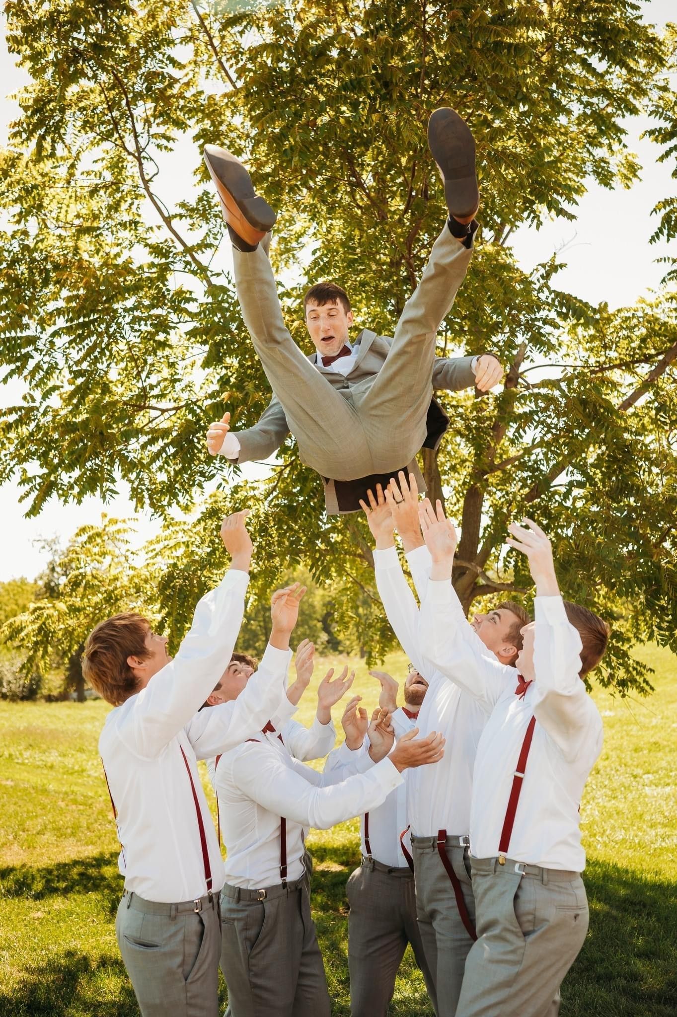 groomsment tossing groom in air in outdoor setting