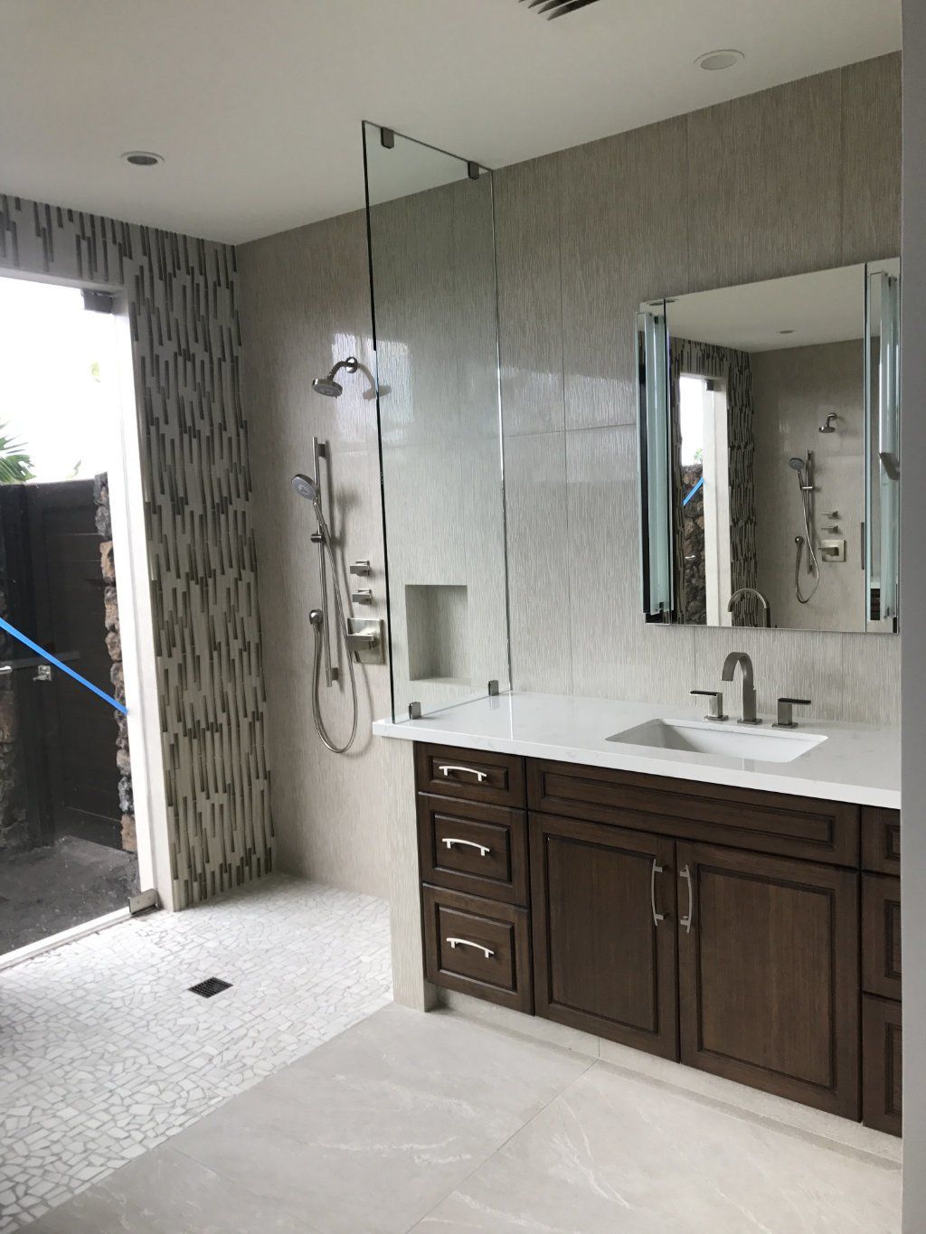 a bathroom with a sink , mirror and tiled shower and wall.