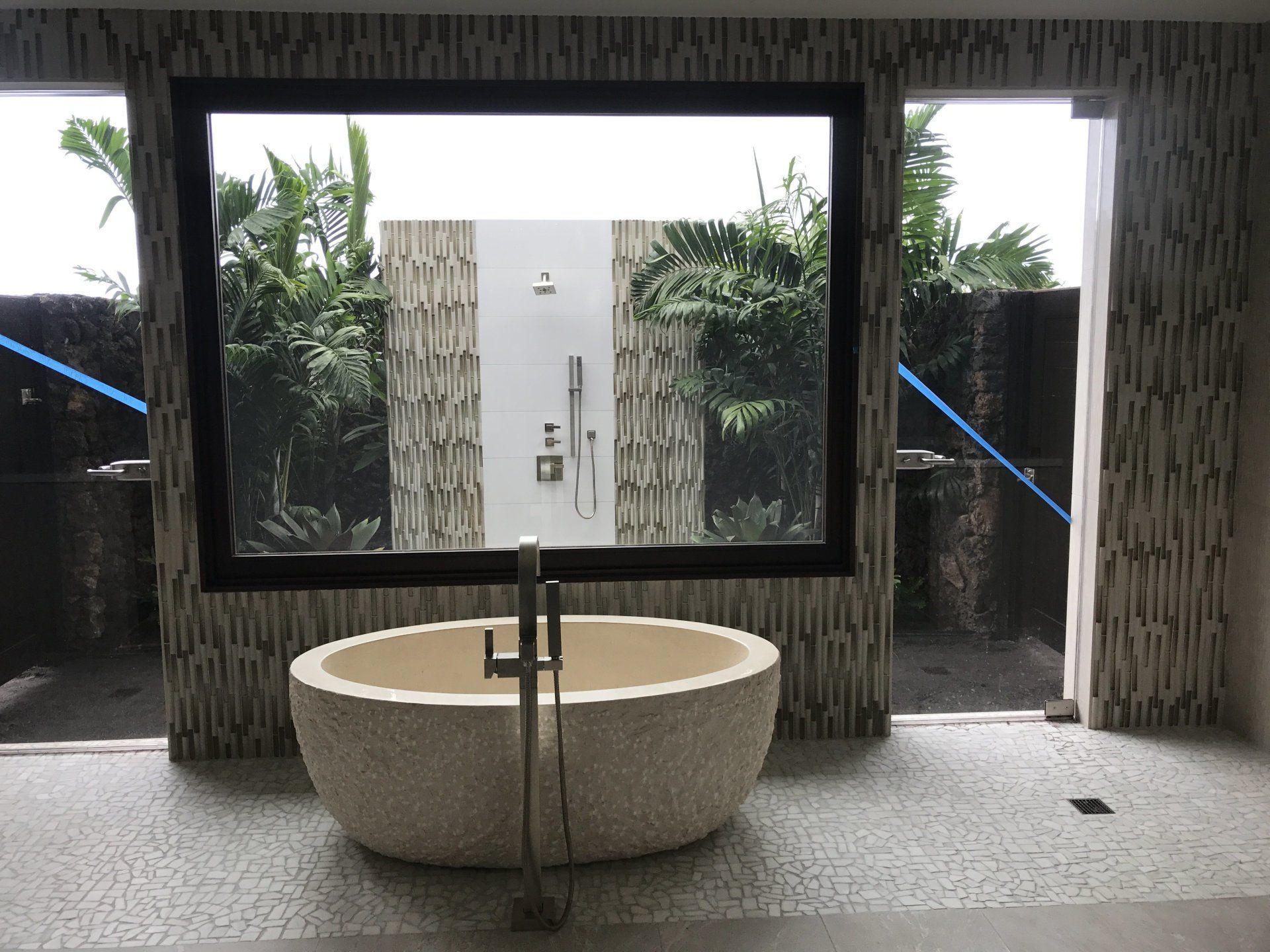 a bathtub in a bathroom with a large window showing tiled outdoor shower. 