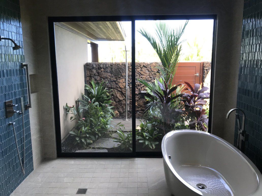 a bathroom with a tiled bathtub and a sliding glass door to outdoor shower. 