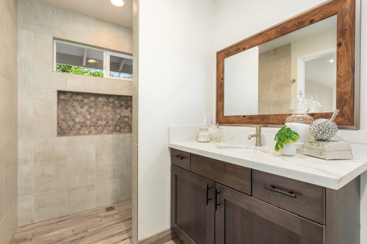 a bathroom with a sink , mirror and tiled walk in shower.