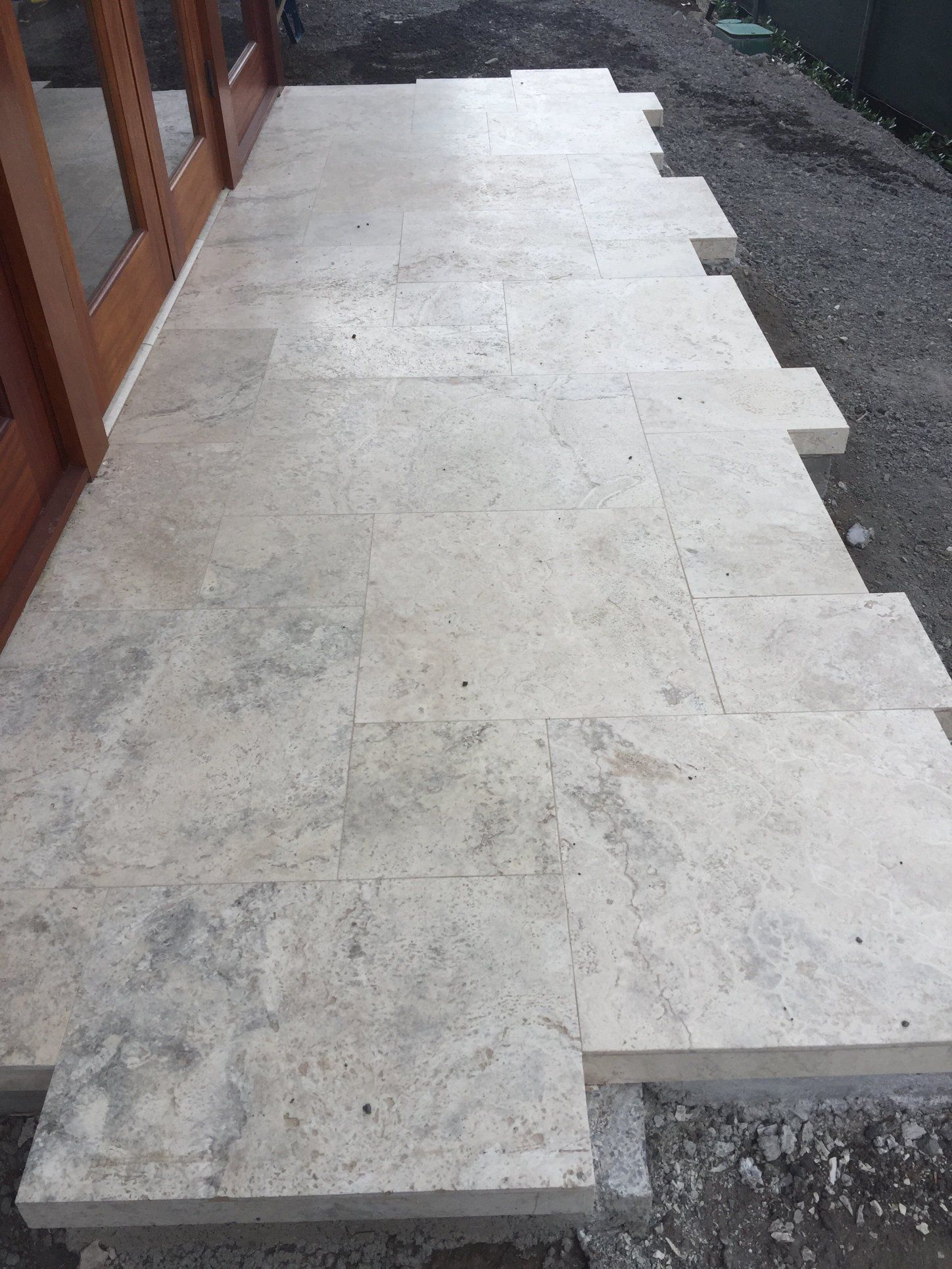 a white stone tile walkway is being built in front of a building .