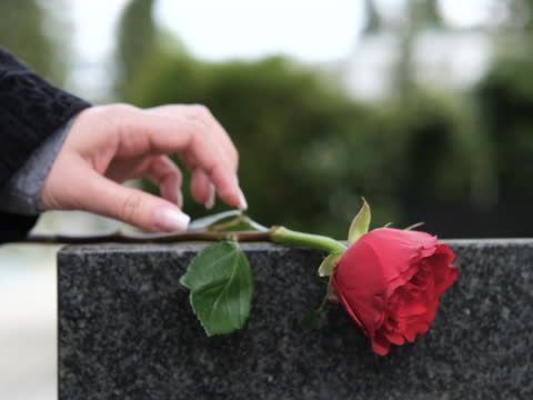 A woman is putting a red rose on a gravestone.