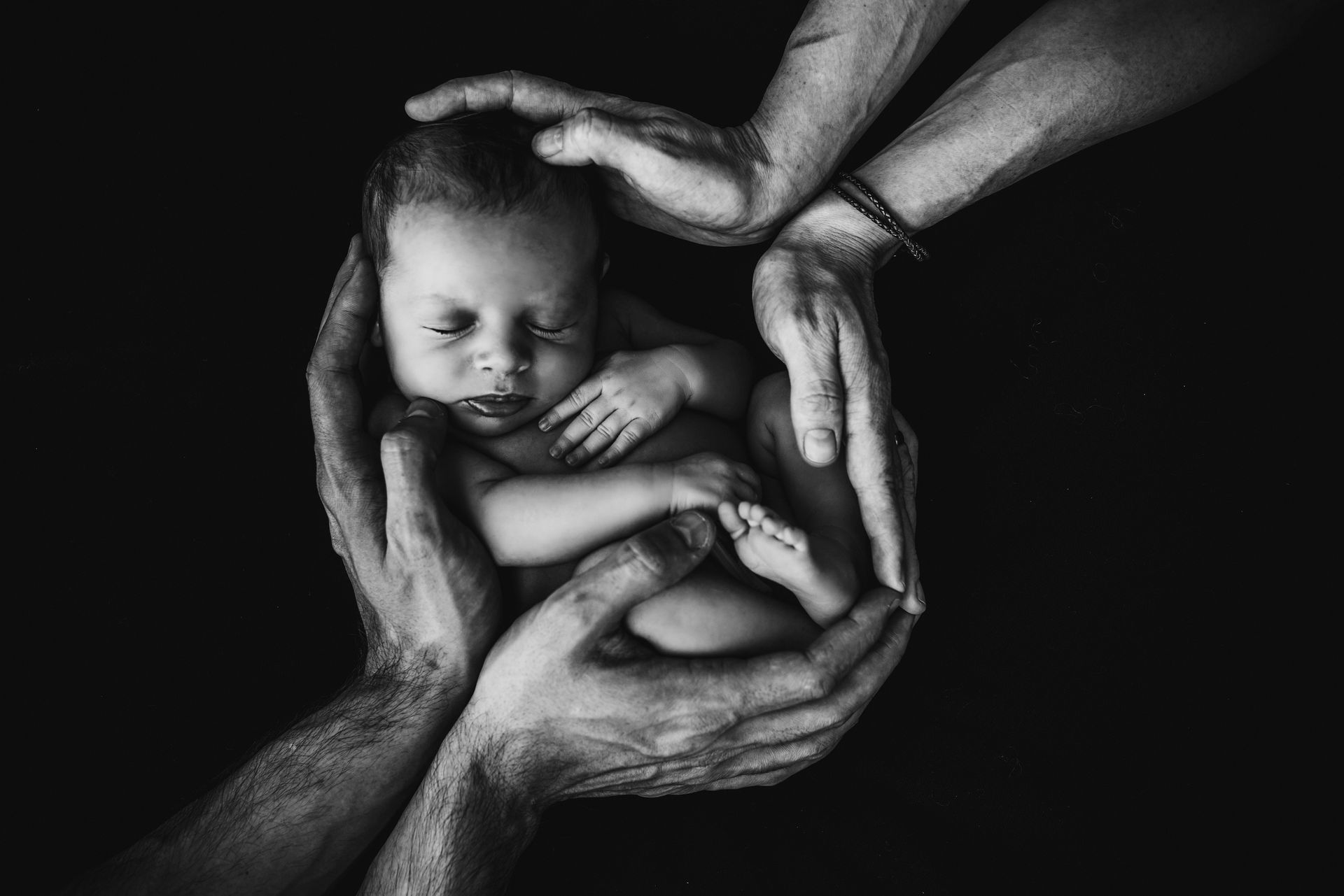 A black and white photo of a newborn baby being held by a family.