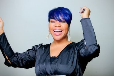 Woman with blue hair and black top, arms raised in excitement.