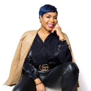 A woman with blue hair is wearing a tan jacket and black pants