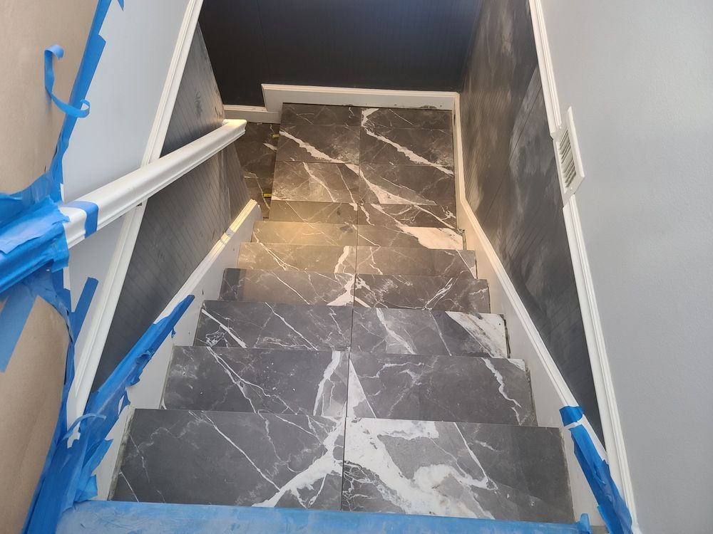 Staircase with gray marble-patterned tiles, white trim, and blue protective tape.