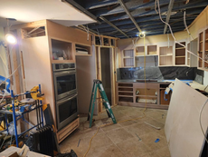 Kitchen under renovation with unfinished cabinets, exposed wiring, and a ladder.