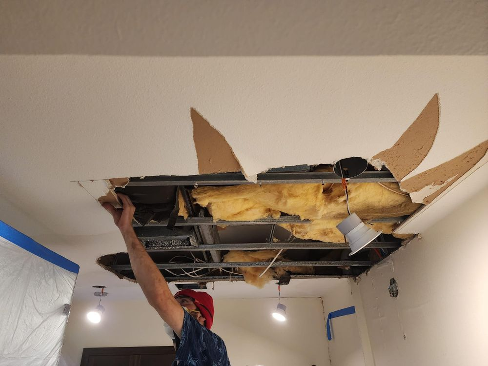 Man reaching up to damaged ceiling with exposed insulation and metal framework.