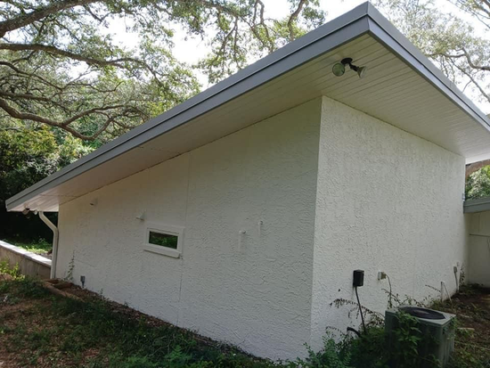 White stucco building with a flat gray roof in a wooded area.